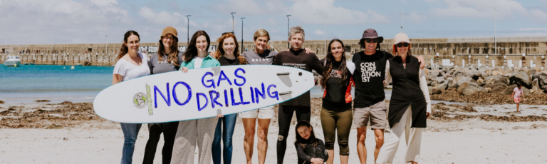 A group of people standing on a beach holding a surfboard with the words 'No gas drilling' written on it