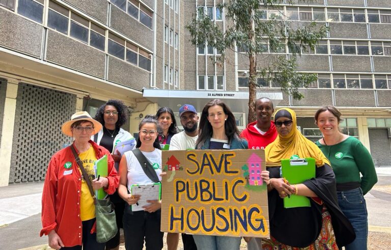 A group of people outside a public housing building with a sign that says 'Save Public Housing'