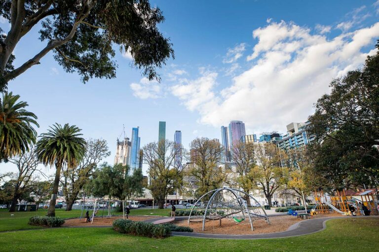 a picture of a park with play equipment and tall city buildings in the background